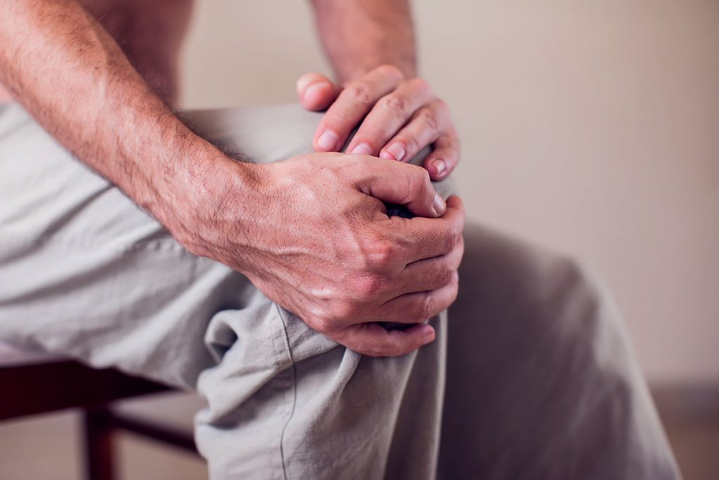 Close up of a man sitting and holding his knee in pain due to injury