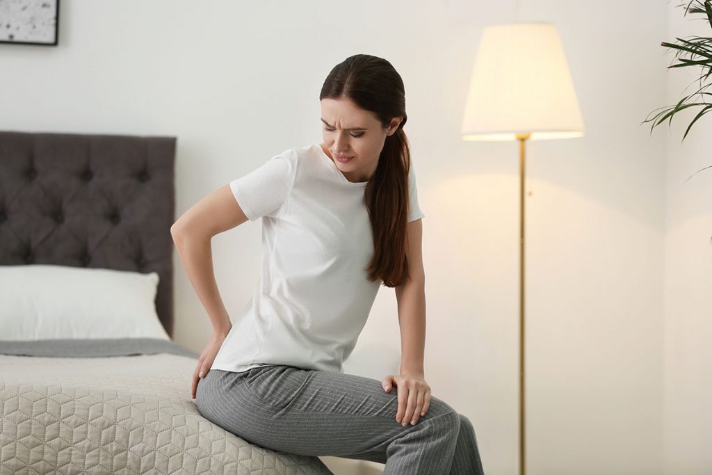 Young woman suffering from Coccyx pain on bed at home